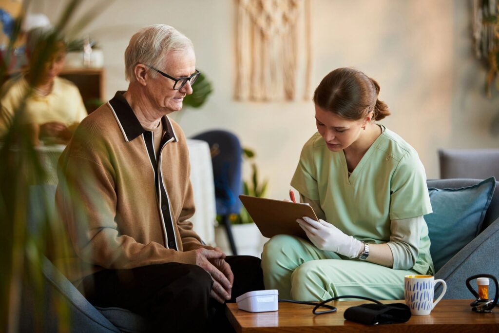 Senior Man Consulting Nurse during Health Assessment in Nursing Home